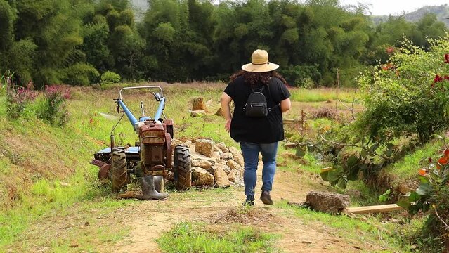 Shot of a woman taking a picture of a tracor in a field.