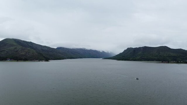 video of aerial shot over the water following a boat, a dam, a river within two mountains in Prado Tolima