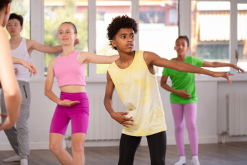 Motivated african american teen boy participating in beginner group ballet class, practicing graceful dance movements in sunlit choreography studio