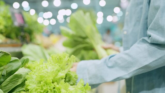 A person is holding a bunch of green vegetables in a store. The vegetables are fresh and healthy, and the person seems to be interested in buying them