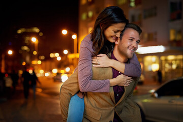 Couple, happy and piggyback in city with love at night for romance, bonding and anniversary date...