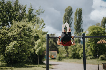 A man displaying strength and skill while working out on a pull-up bar at a public park, with green trees and a clear sky in the background.