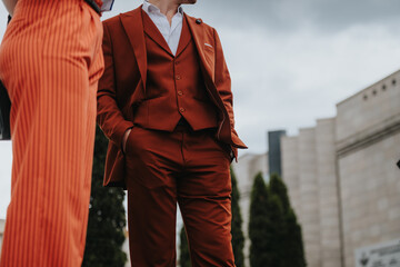 Fashionable individuals in red suits standing outdoors showcasing stylish business attire. Modern...