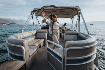 A happy, joyful girl raises her arms in celebration while standing on a pontoon boat, surrounded by beautiful mountain and water landscapes.