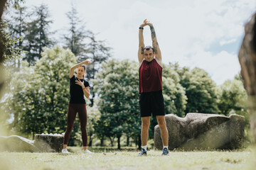 A man and woman engage in stretching exercises in a lush park, enhancing their fitness under a...