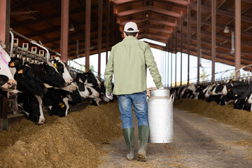Male farmer carries a large milk can in his hands at a cow farm