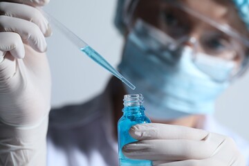 Scientist dripping liquid from pipette into glass bottle on light background, closeup