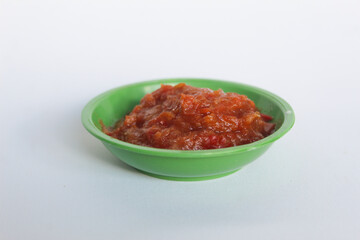 Portrait of tomato chili sauce in a green bowl isolated on a white background.
