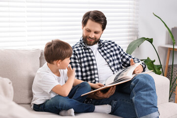 Happy dad and son reading book together on sofa at home