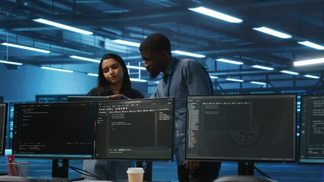 Multiethnic team of engineers uses laptop to do programming for servers providing computing resources for different workloads. Diverse colleagues using notebook to supervise data center supercomputers