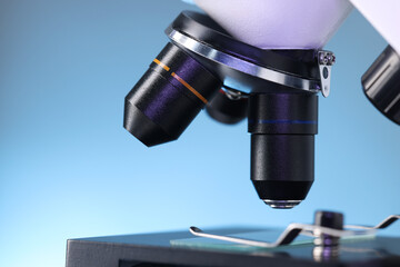 Modern microscope on light blue background, closeup view