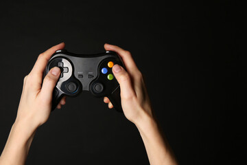 Woman using game controller on black background, closeup. Space for text