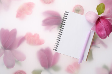 Guest list. Notebook, pen and magnolia on spring floral background, flat lay. Space for text