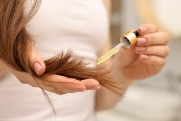 Woman applying oil hair mask indoors, closeup