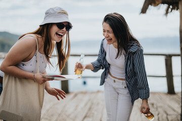 Two happy female tourists sharing a laugh and a drink during a leisurely trip by the lakeside,...