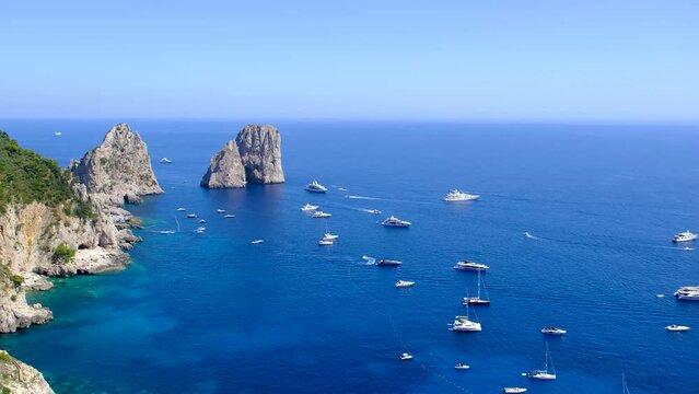 Luxury yachts by Faraglioni di Capri. Boats take tourists to the famous Faraglioni di Capri, Italy.