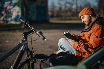 A relaxed urban reader takes a break outdoors, immersed in literature, with his bike parked...