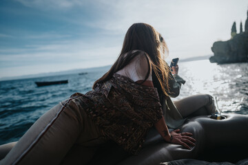 A joyful young girl on a boat captured from behind, overlooking a serene sea while holding a smart...