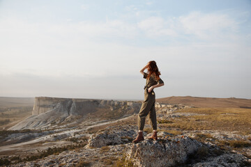 Woman standing proudly on rock in desert landscape with hands on hips, travel adventure and...