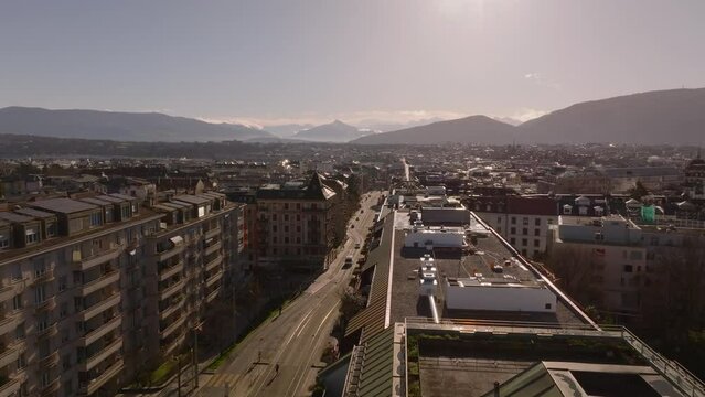 Aerial view of a vibrant city with traffic street in Geneva during sunset, featuring buildings and mountains in the distance