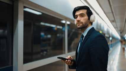 Project manager wearing headphone at train station while holding mobile phone for choosing song....