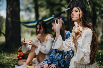 Three young women, likely sisters, are seen enjoying a peaceful picnic in a lush park, eating...