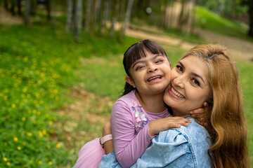 Fototapeta premium Woman carrying a child with Down syndrome outdoors in a public park in the city
