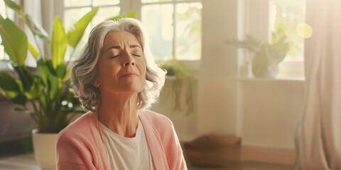 Fototapeta premium A middle-aged woman sits near a window in her home, meditating with her eyes closed, looking happy and content as sunlight streams in.