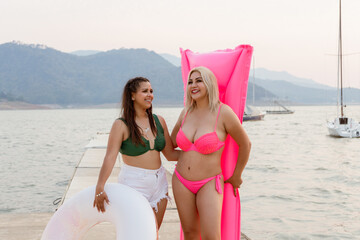 Two Women with Inflatable Float and Mattress on Lakeside Pier - Powered by Adobe