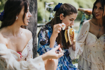 A joyful outdoor gathering of three sisters in a park, eating bananas and enjoying each other's...