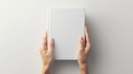Two hands holding a blank white book against a plain background, offering a minimalist scene that's ready for text or graphic customization.