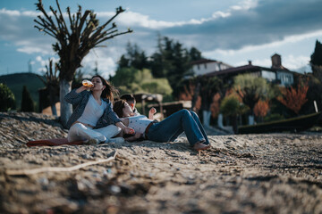 A young couple relaxes on a sandy beach, enjoying a moment together with a glass of wine, surrounded by serene nature and quaint buildings.