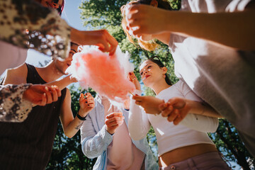 A group of young adult friends enjoy a sunny day in the park, sharing pink candy cotton, embodying...