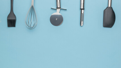 Modern Kitchen Utensils on Blue Background: Whisk, Spatula, Pizza Cutter, Peeler, Brush