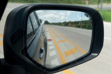 Abstract mirror wing of car. Looking back for trip yellow line in center of road. Under blue sky in...
