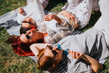 Group of young friends lying back on a blanket in the park, enjoying the sun and playful moments...