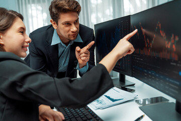 Two business traders discussing on dynamic stock market in currency rate investment trading on two pc screens with compare real time graph on risk or profit point of data at modern office. Postulate.