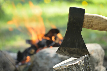 Hatchet embedded in a log of wood opposite campfire