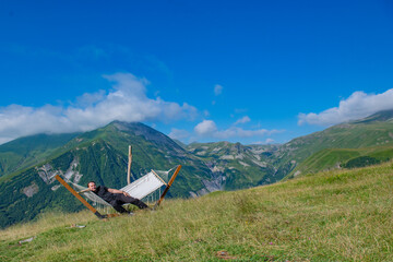 Seeking Solitude: Man Wearing Black Attire Lounging in Hammock with Scenic Mountain and Sky View