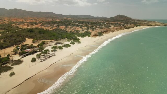Aerial panning shot of sandy beach on Margarita Island, Macanao during sunny day. Waves reaching island shore. Wide shot.