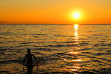 夕暮れの逗子海岸、夕陽を見ながら海遊びをする人のシルエット