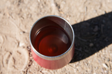 Looking down at fresh tea in red cup outdoors, made while camping.  