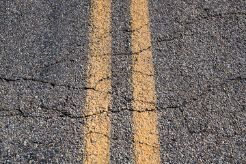 Solid yellow lines on road with cracks on desert highway.