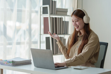 Young Asian woman looks happy wearing headphones Watch the webinar Listen to online courses...