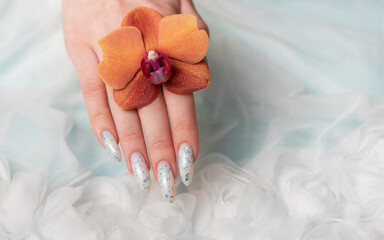 Showcasing Floral Nail Art and Holding an Orange Blossom on a Soft Textured Surface