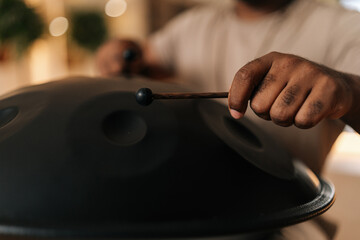 Close-up hands of unrecognizable black male in trance playing meditative instrument tank drum using...