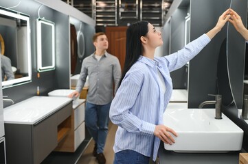 Young couple choosing new bathroom furniture at the plumbing shop with lots of sanitary goods