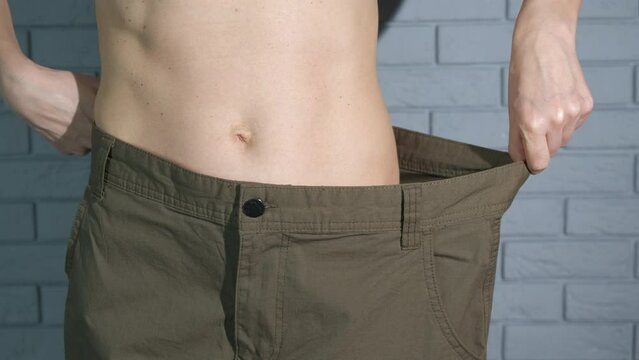 Oversize lady jeans on slim body. A view of slim female body in oversize jeans by the wall.