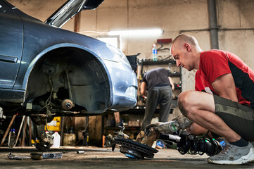 Fototapeta premium Repairman, worker fixing car. Hardworking man working in garage, servicing auto center, repairing automobile. Concept of manal men work.
