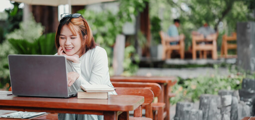 A woman is sitting at a table with a laptop and a book. She is smiling and she is enjoying her time. The scene suggests a relaxed and leisurely atmosphere